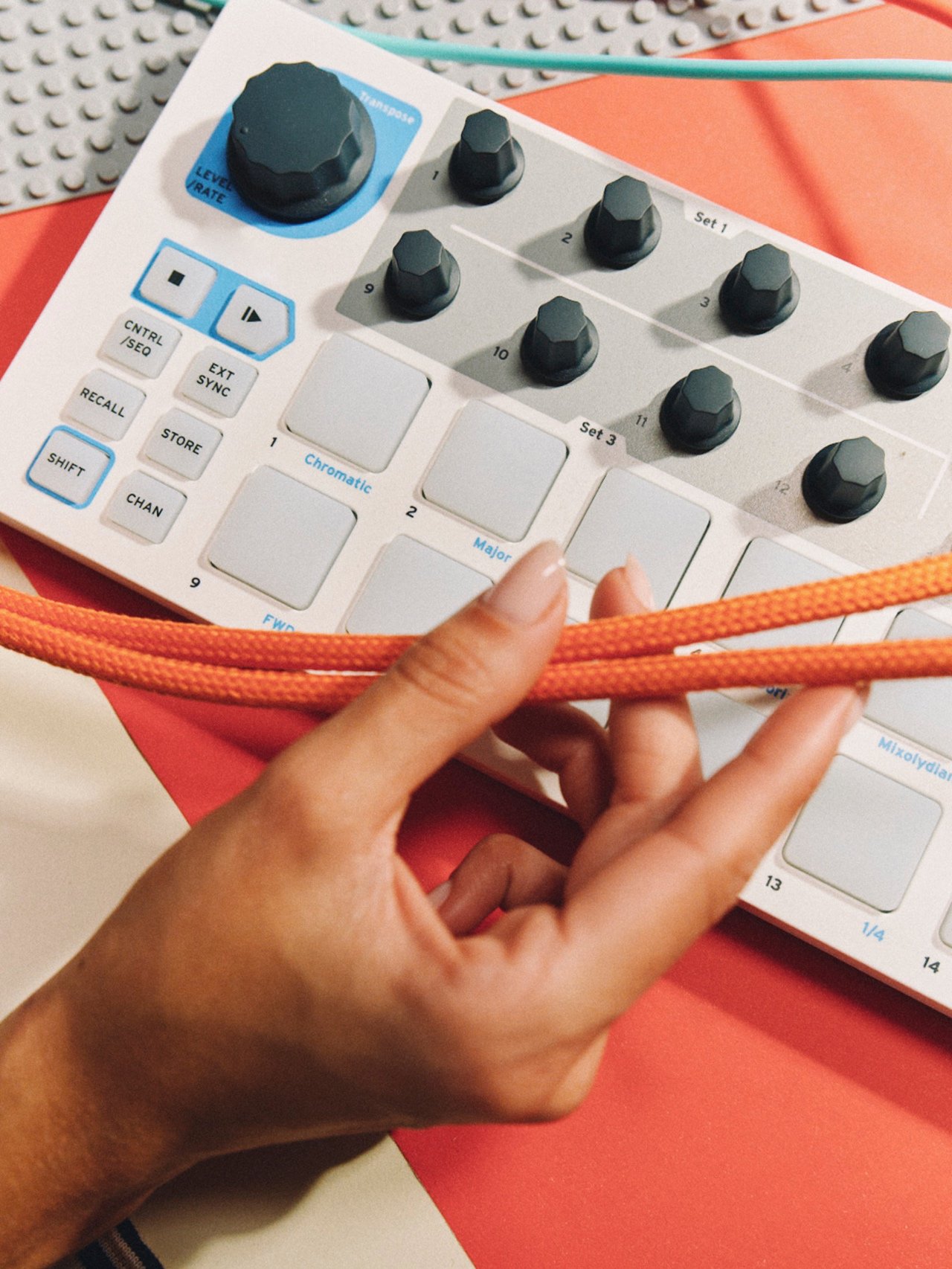 Close-up of a hand, an orange cable, and a music control surface.