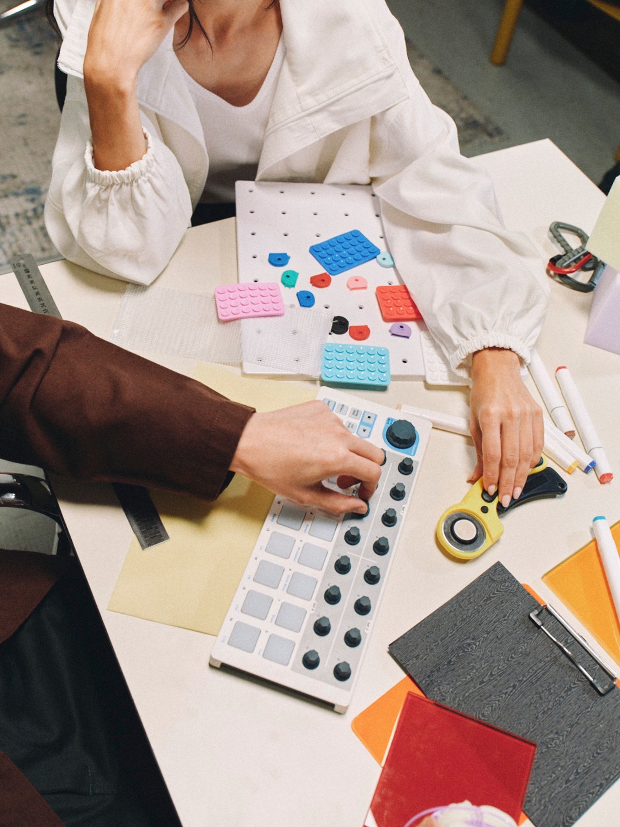 Overhead view of two people working with prototypes and a music controller.