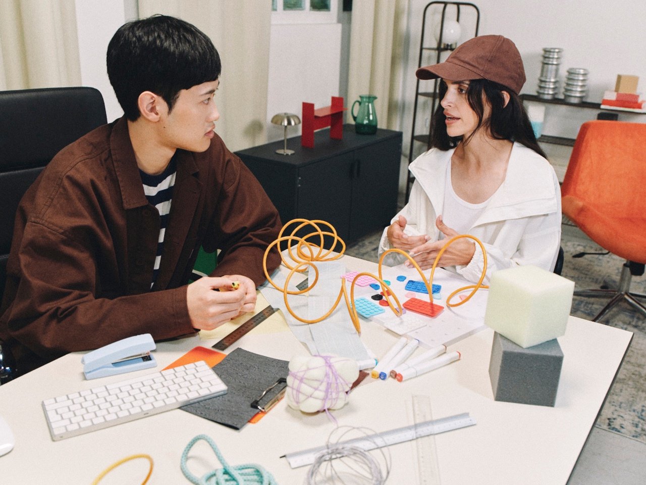 Two people discussing colorful prototypes at a shared studio table.